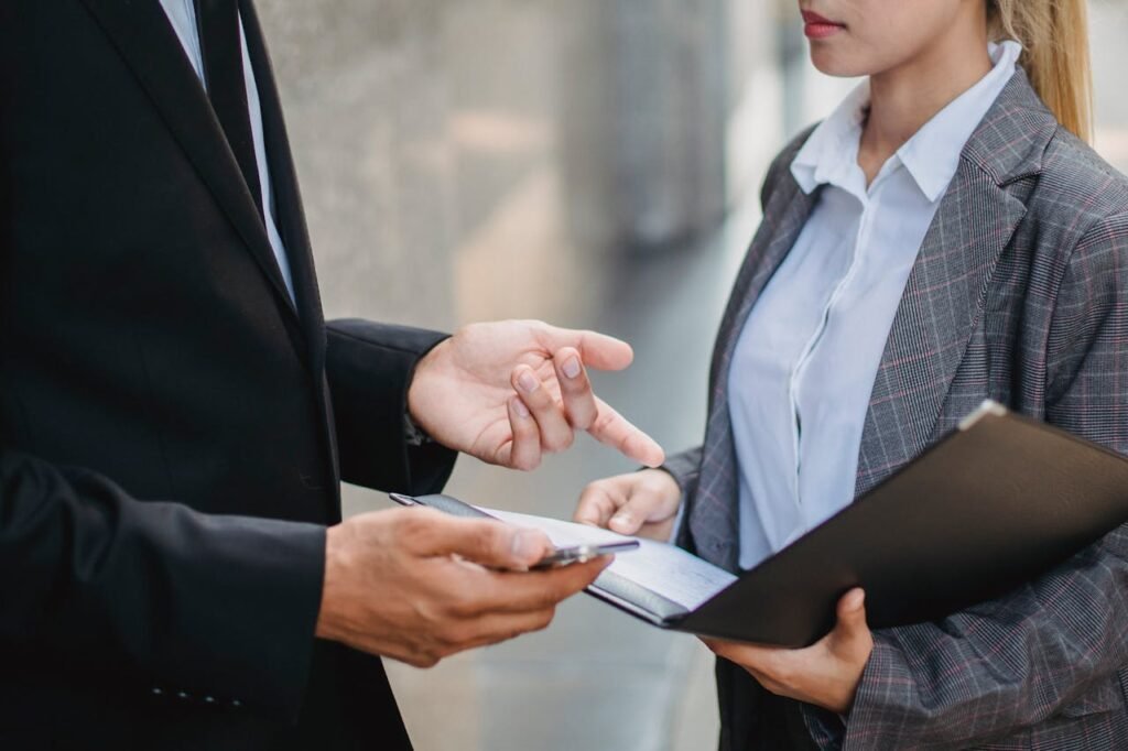 pexels-photo-4963438 A businessman and businesswoman in formal attire engage in a focused discussion outdoors.