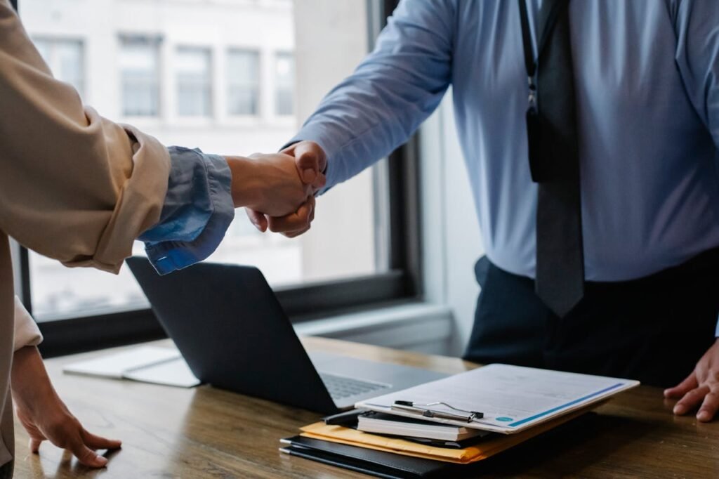 pexels-photo-5673488 Crop unrecognizable coworkers in formal wear standing at table with laptop and documents while greeting each other before meeting